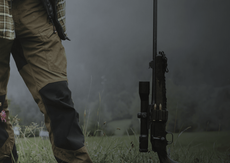A person firing a rifle with visible smoke from the barrel.
